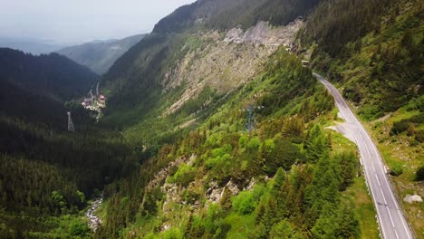 Drone aerial view over Transfăgărășan, winding road, Balea lake lodges, rocky cliffs and mountain mist.