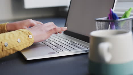 midsection of biracial woman sitting at desk using laptop with copy space at home, slow motion