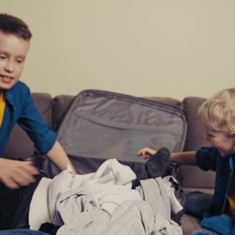 cheerful boys and a valise with different clothes on the couch in the room. two happy brothers taking the things out of a suitcase at home.