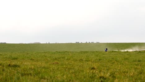 Motociclista-Todoterreno-Cabalgando-A-Través-Del-Bastidor-Entre-Dos-Prados-Verdes