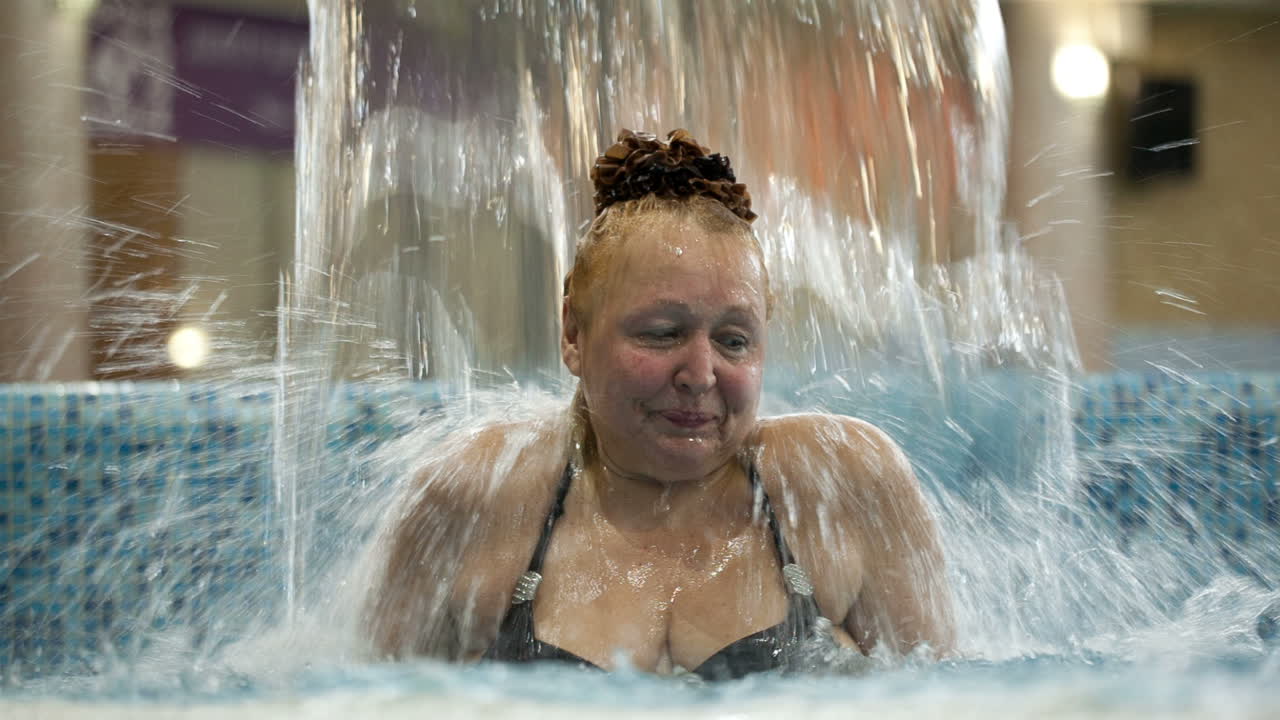 Donna di mezza età sotto un getto d'acqua in piscina