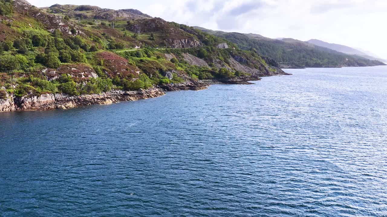 Drone glides over rugged Scottish coastline, capturing cliffs, blue ocean, and a soaring seabird