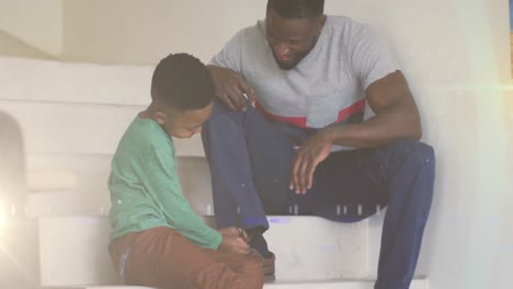 animation of lights over happy african american boy tying shoes to father