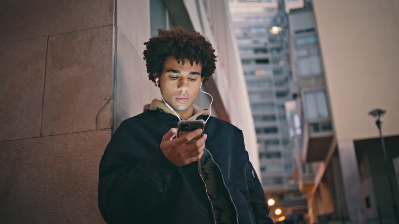 Cool hipster using smartphone at evening street in earphones closeup.