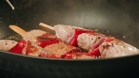 cooking chicken skewers in a pan