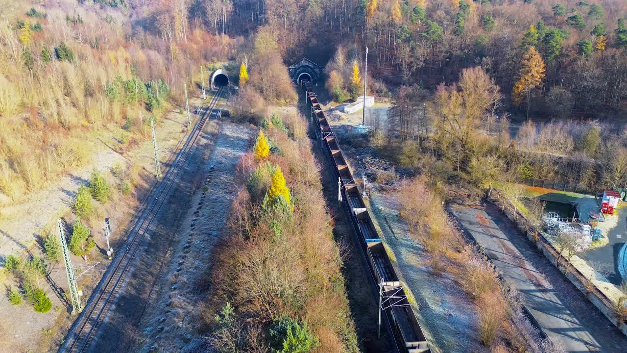 Freight train entering dual railway tunnels in bright winter landscape captured from aerial perspective