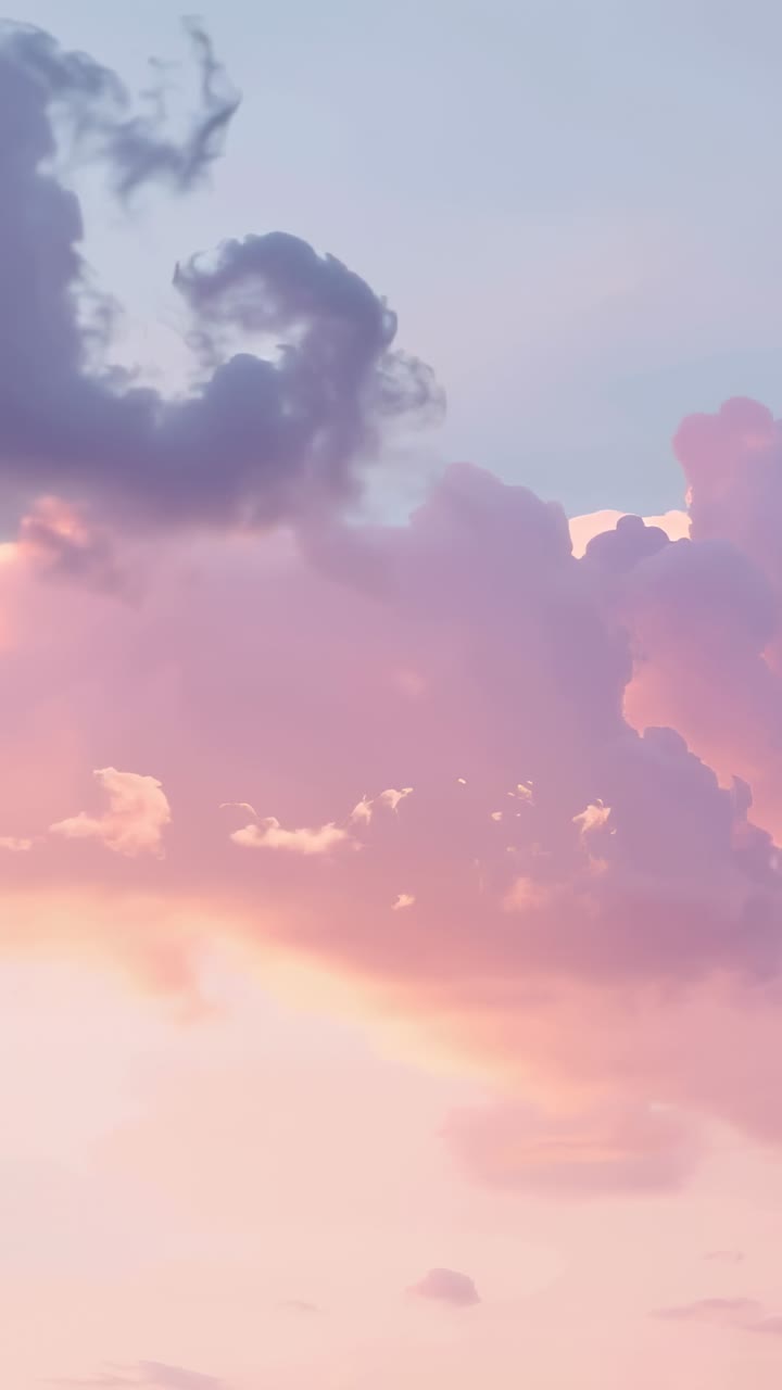 Video verticale: Massa di cumuli rosa alla deriva che si sposta durante il tramonto, una nuvola sottile più scura che entra da sinistra.