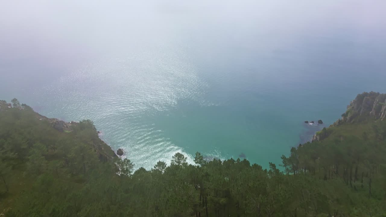 Drone ascends over trees and mist, revealing Île Vierge Beach on Crozon Peninsula, Brittany, with cliffs, vegetation, and sea view. France