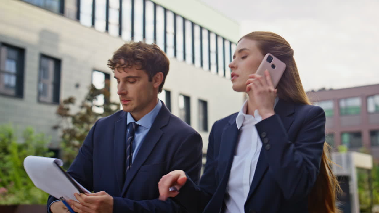 Lady boss talking cellphone walking with man secretary at city street closeup