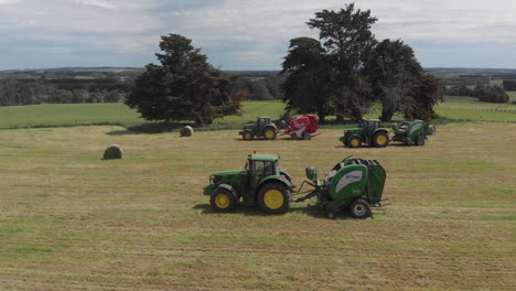 Lado-Aéreo-Después-De-La-Toma-De-3-Tractores-Conduciendo-En-El-Paddock-Haciendo-Pacas-De-Heno