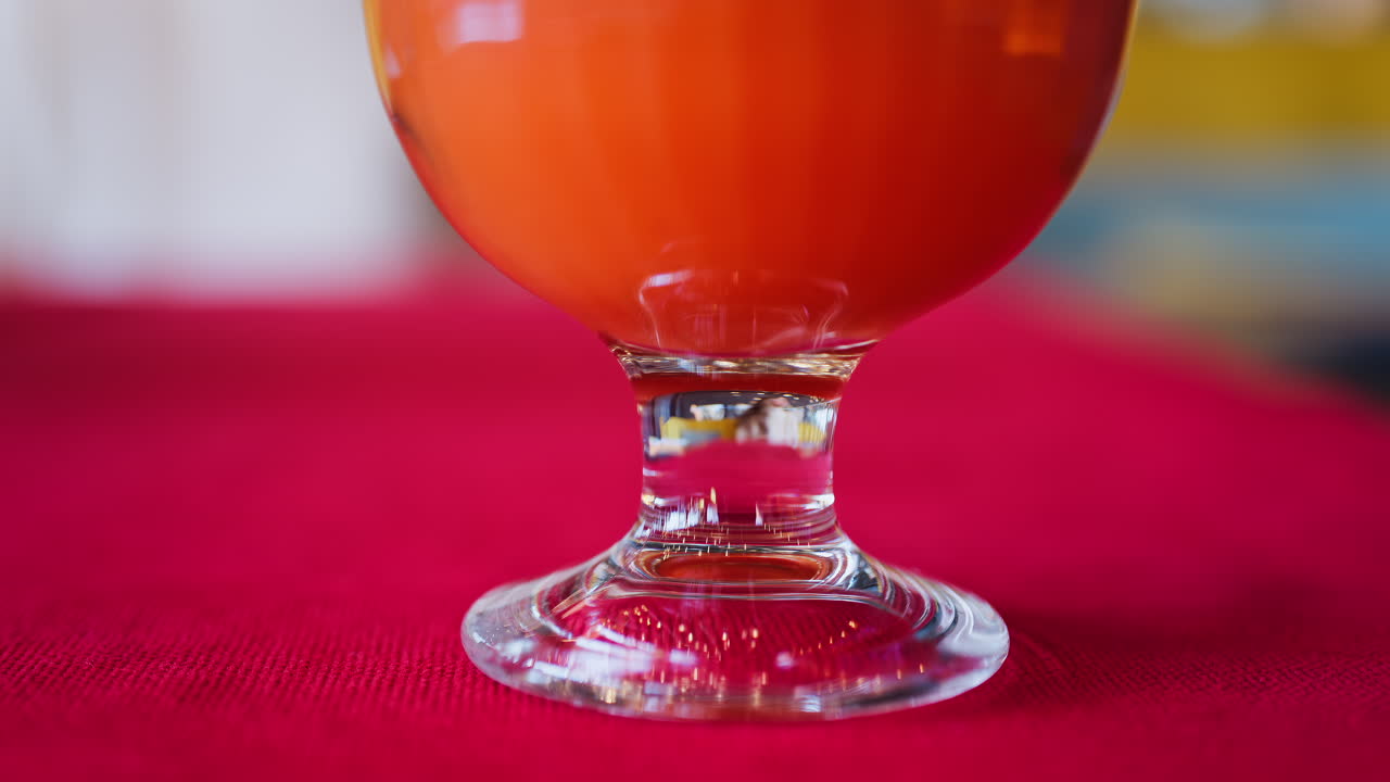 Close up of an orange and carrot juice in a glass with a black straw on a red table cloth