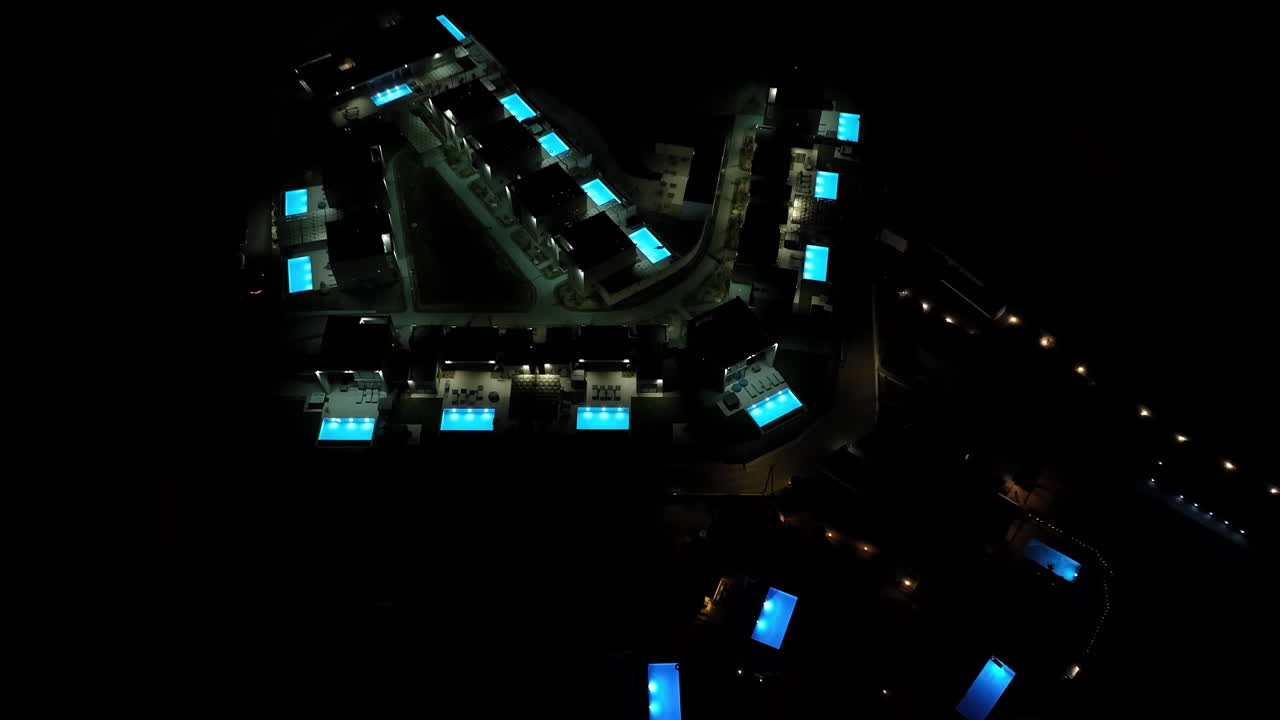 Aerial view tilting backwards over illuminated pools and villas, night in Greece
