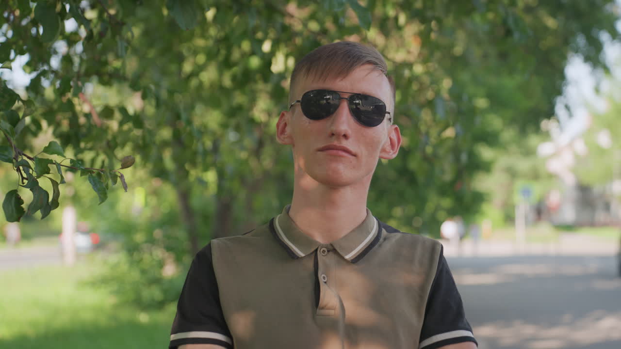 Calm Guarded Stance, Serene Man Under Shady Tree, Quiet Man Adopts Defensive Posture Outdoors, Unemotional Individual With Sunglasses And Crossed Arms Reveals Subtle Tension And Guarded Mindset