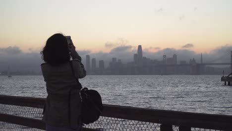 young women taking a photo of san francisco during a peaceful evening by the bay