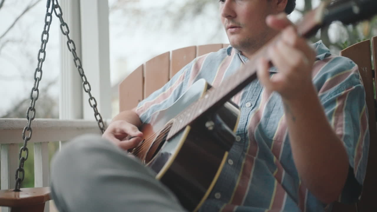 Man Playing Acoustic Guitar on a Porch Swing