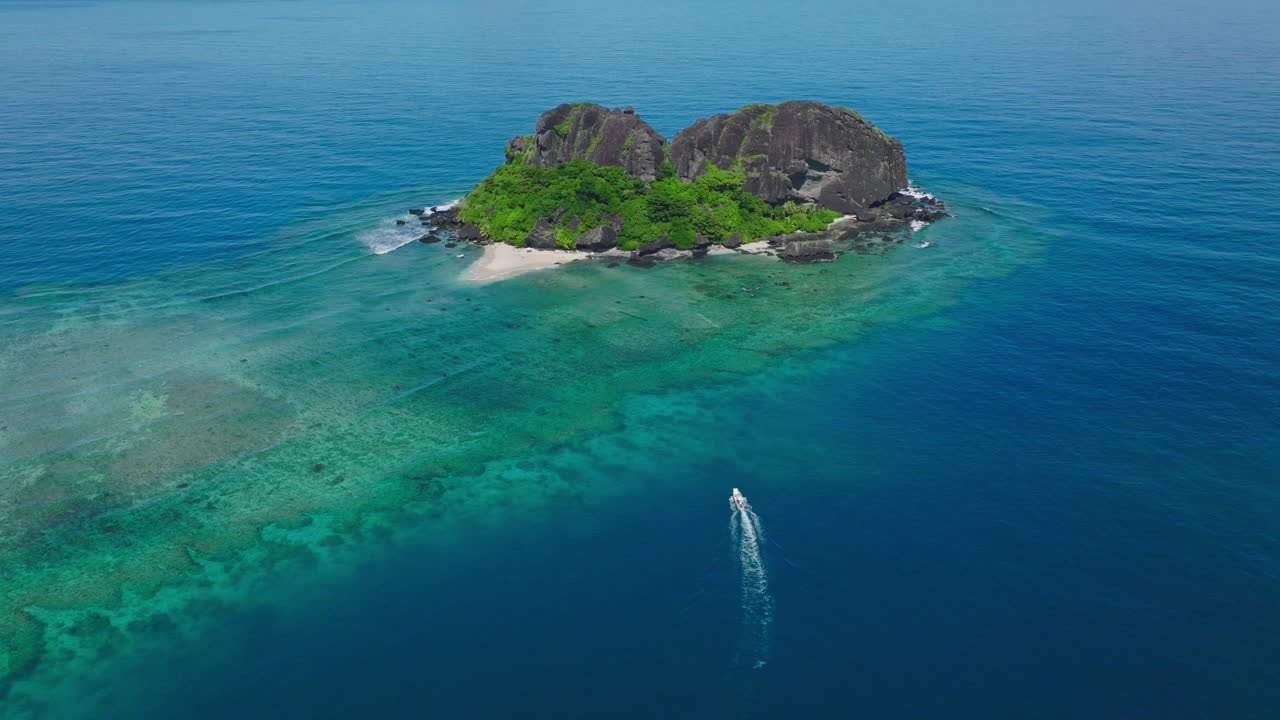 Drone orbiting vibrant tropical island reef with boat wake in water below