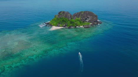 drone orbiting vibrant tropical island reef with boat wake in water below