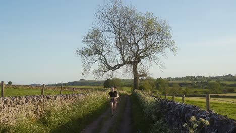 zooming out wide shot of young blonde woman jogging along dirt track in peak district