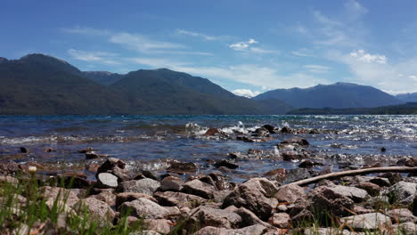 waves wash over stones by forested andes mountains, static ground view