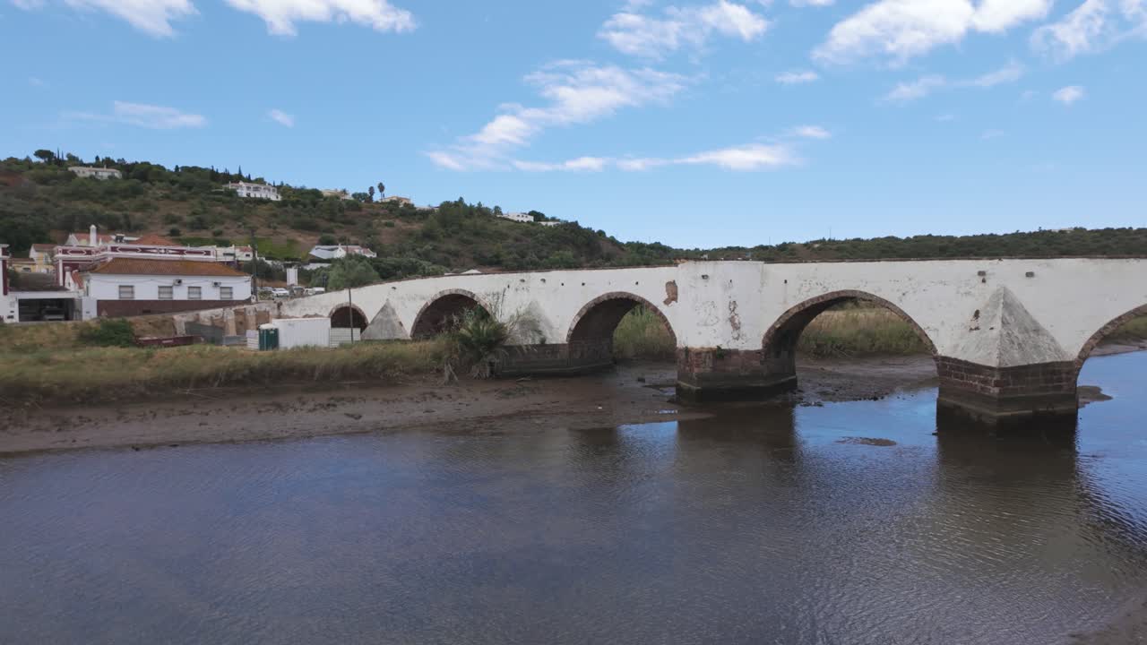puente romano en silves, portugal, cruzando un río tranquilo con colinas en el fondo