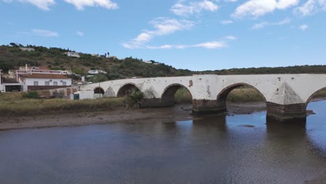 roman bridge in silves, portugal, crossing a calm river with hills in the background