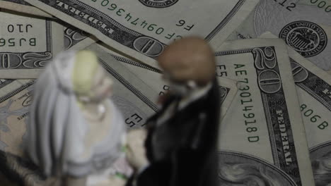 a married couple figurine stands amid twenty dollar bills