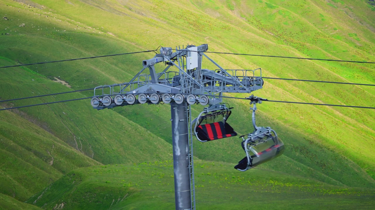 Seggiovie e cabinovie che superano un pilone di impianto di risalita su una montagna verde