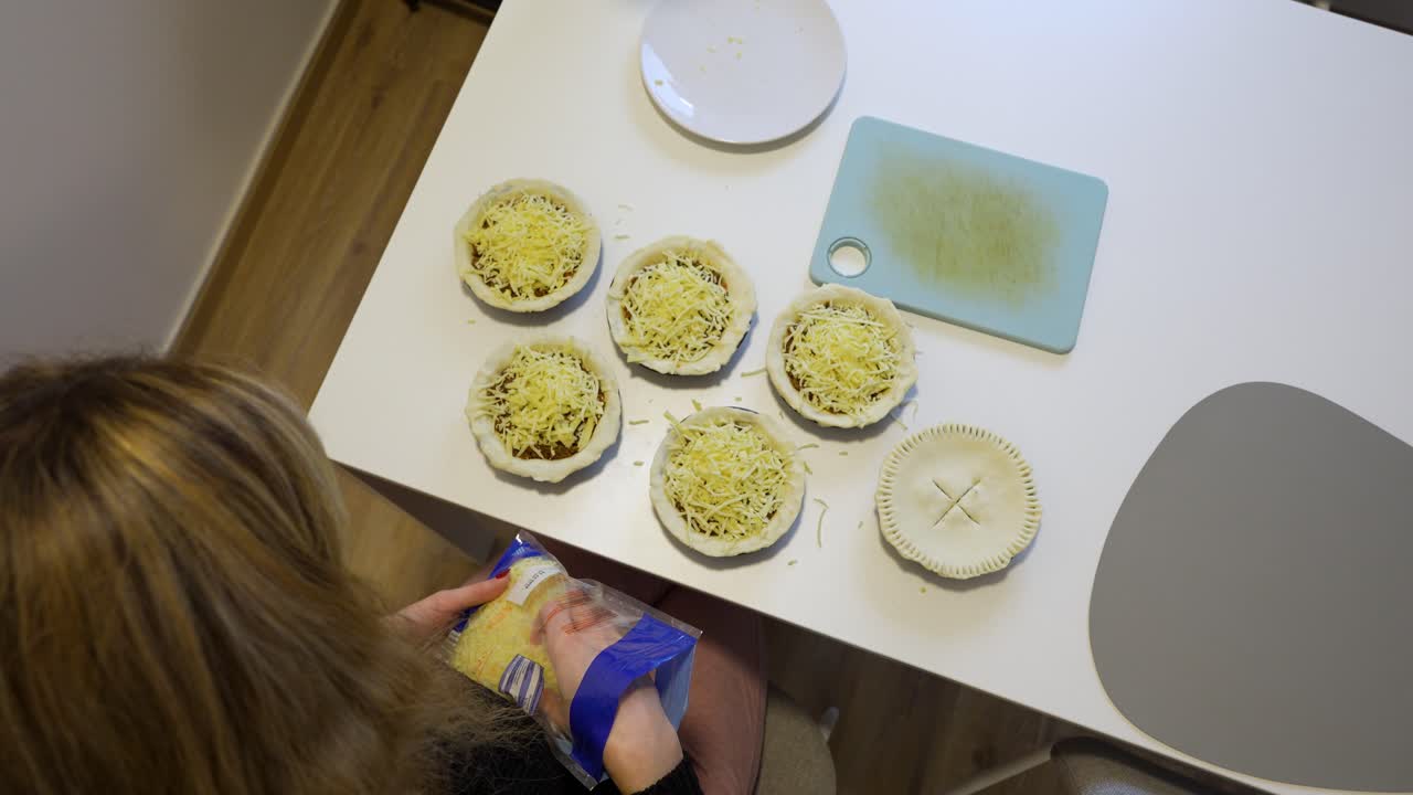 Woman Putting Cheese On Top Of Meat Pies. - high angle shot
