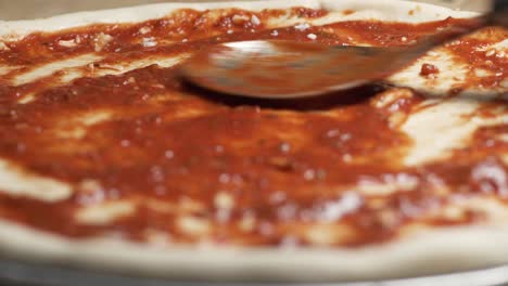 Hand-of-talented-chef-finishing-sprinkle-mozzarella-on-a-pizza-dough-with-juicy-red-sauce-placed-on-a-steel-tray-on-a-wooden-counter