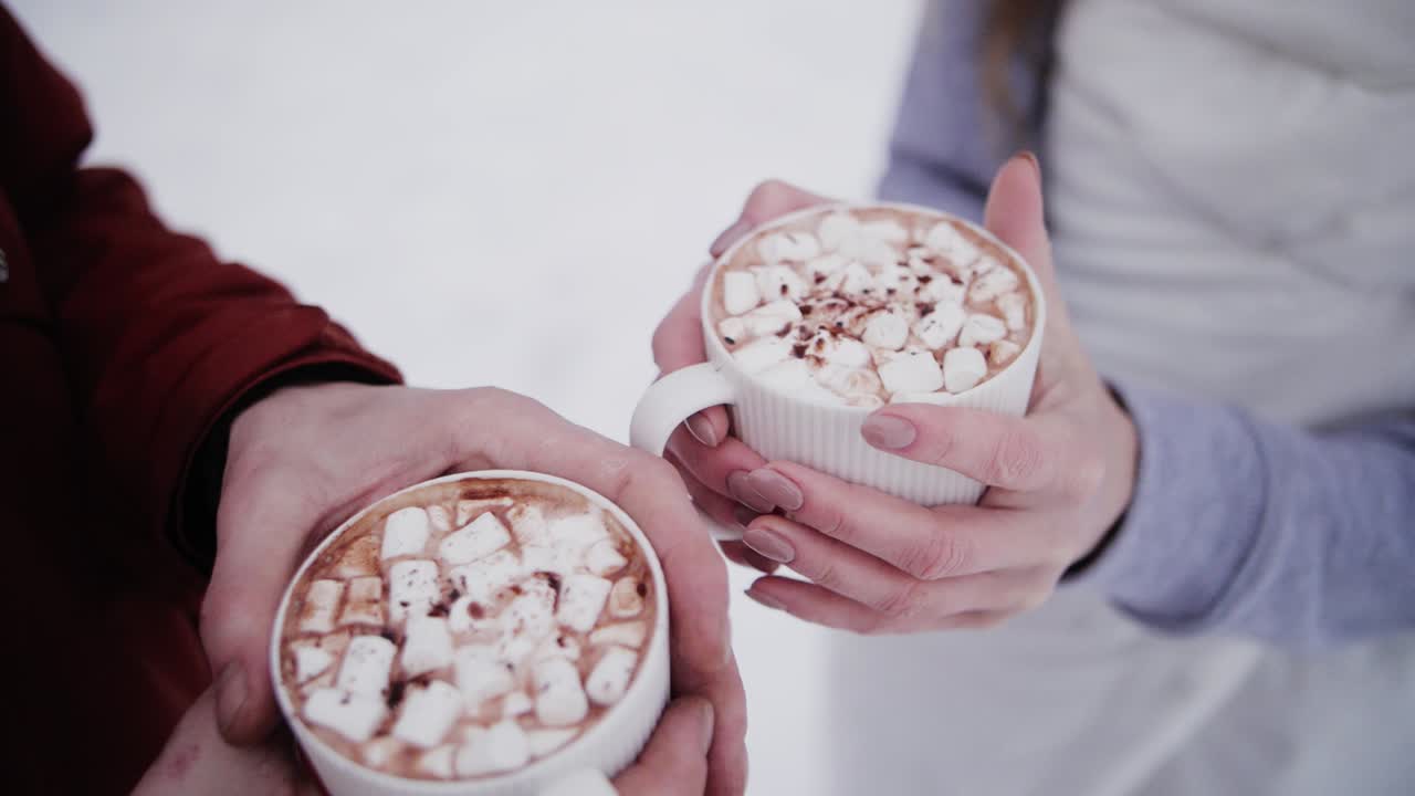 Due tazze di cacao in mani che si scaldano con marshmallow in inverno e neve sullo sfondo