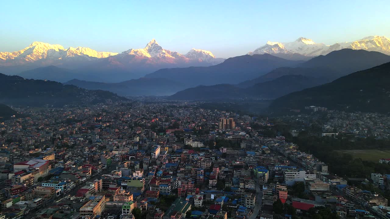 Aerial view of Pokhara city at sunrise with golden light illuminating the Annapurna range and Machhapuchhre peaks, showing the valley’s urban landscape framed by majestic Himalayas