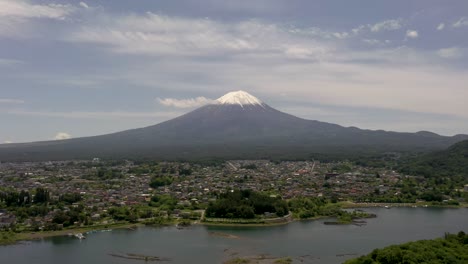 Vuelo-Aéreo-Por-Encima-Del-Lago-Kawaguchi-Con-El-Monte-Fuji-Reflejándose-En-El-Agua,-El-Paisaje-Escénico-Y-El-Pico-Nevado-En-Un-Día-Claro-Y-Soleado-En-Fuji,-Japón