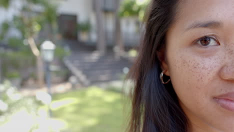 Half-face-of-asian-woman-standing-and-smiling-in-sunny-garden,-slow-motion,-copy-space