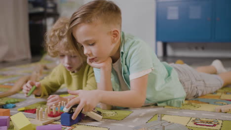 two little boys playing with wooden pieces and car lying on a carpet in a montessori school class