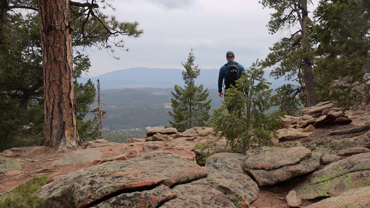 One male hiker walks out to a remote mountain overlook in windy conditions. Filmed in Staunton State Park during the spring.