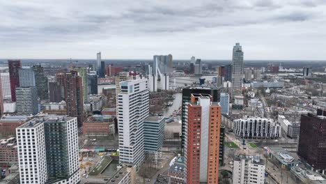 the drone is flying over tall buildings with the erasmus brigde in the background an a cloudy day in rotterdam the netherlands aerial footage 4k