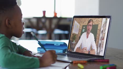 niño afroamericano haciendo la tarea mientras tiene una videollamada con un profesor masculino en una computadora portátil en casa