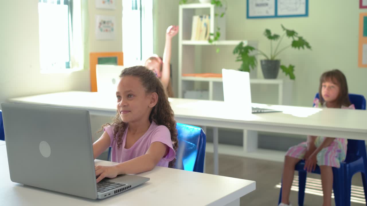 Bambina che alza la mano sentendo la domanda dell'insegnante e digita sul laptop in classe, alzando lo sguardo