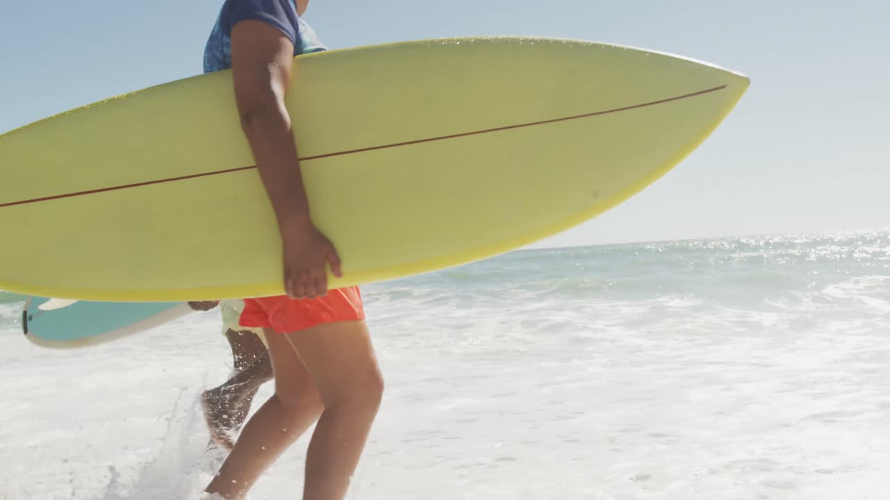 pareja afroamericana de alto nivel corriendo con una tabla de surf en una playa soleada