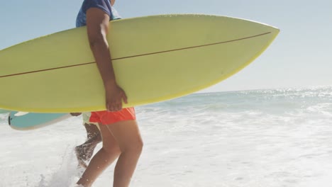 senior african american couple running with surfboard on sunny beach