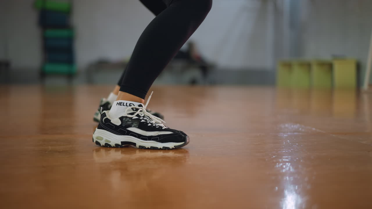 Close view of legs in black leggings and sneakers bouncing on polished wooden floor in fitness studio, capturing energy, rhythm, and dynamic movement during active workout with focus and control