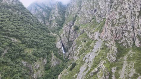 Disparo-De-Drone-De-Una-Cascada-En-Medio-De-Montañas-Caucásicas-Con-Nubes-De-Rocas-Y-árboles-Verdes-Y-Niebla