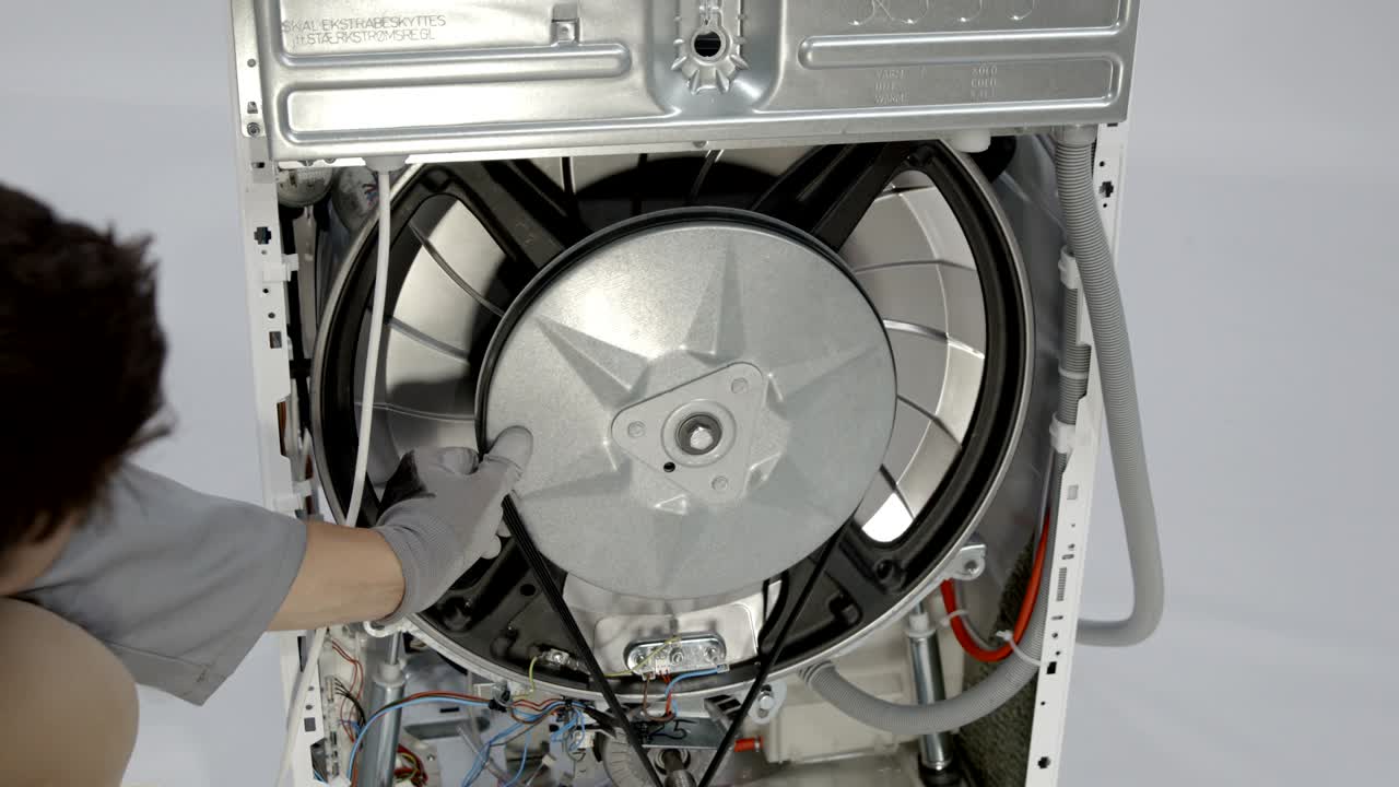 수리 직원이 세탁기의 변속기에서 벨트를 제거하고 있습니다.