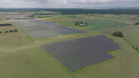 Una-Pequeña-Racha-De-Luz-Solar-Llega-A-Un-Enorme-Parque-Solar-En-El-Paisaje-Rural-De-Suecia,-Aéreo