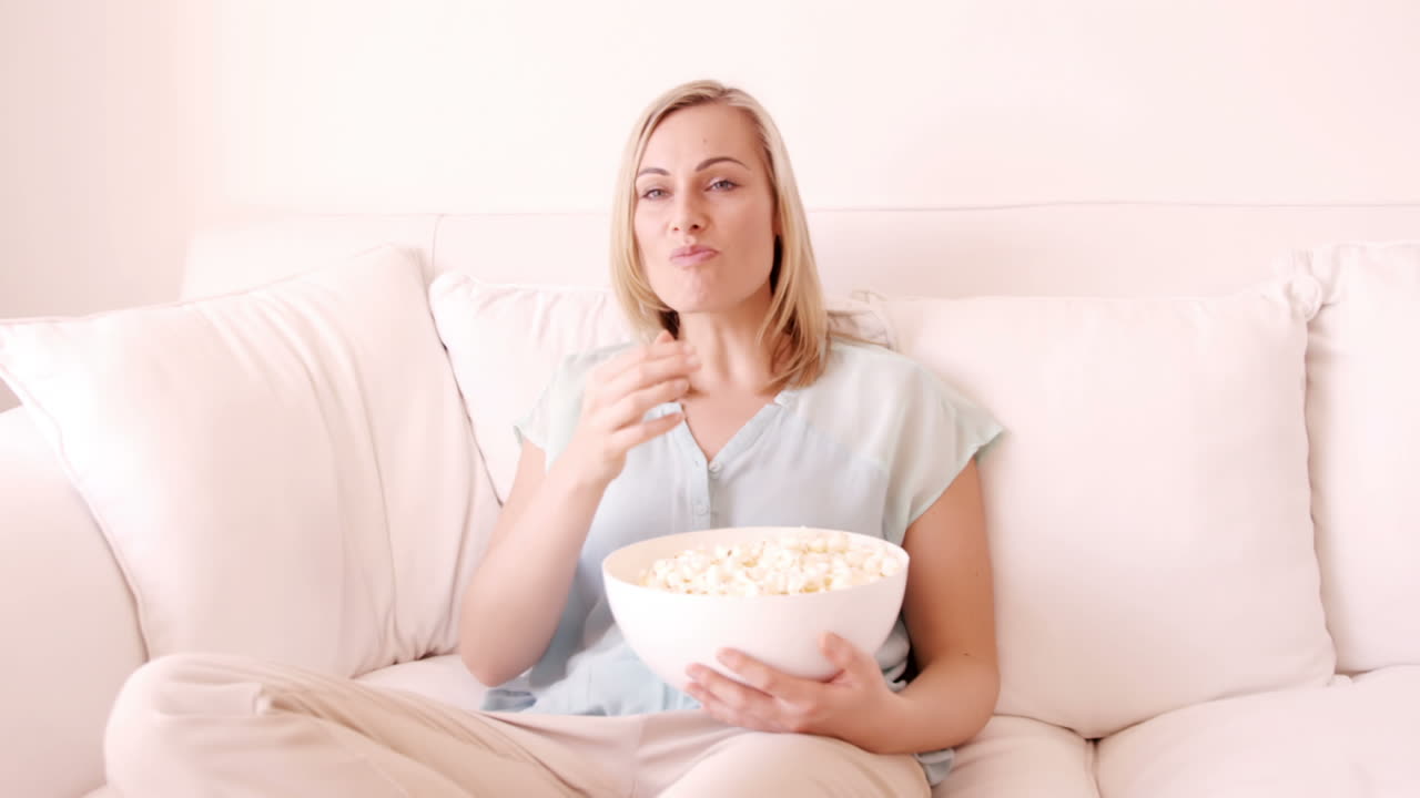 mujer rubia sentada en un sofá y comiendo palomitas de maíz