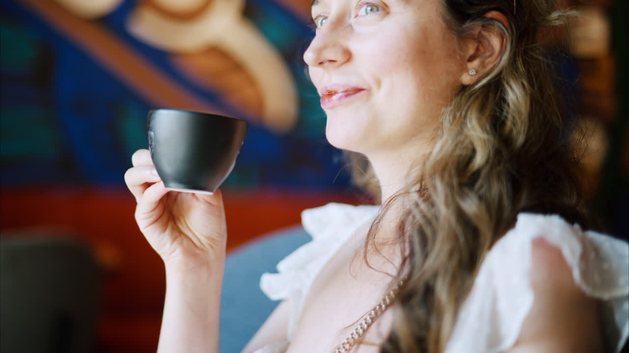 Brunette woman in white dress drinking a coffee at a cafe in daylight