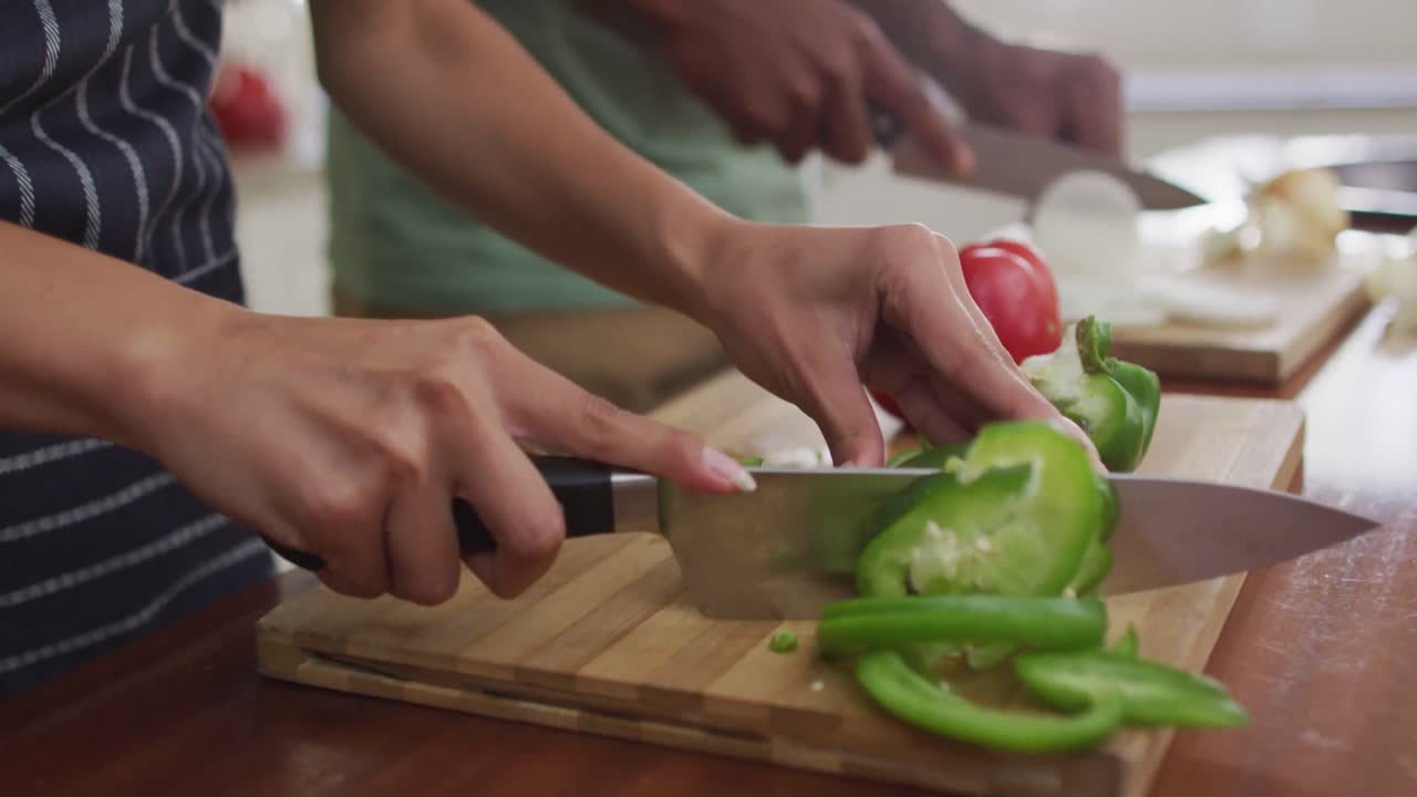 manos de una pareja biracial cocinando juntos, cortando verduras
