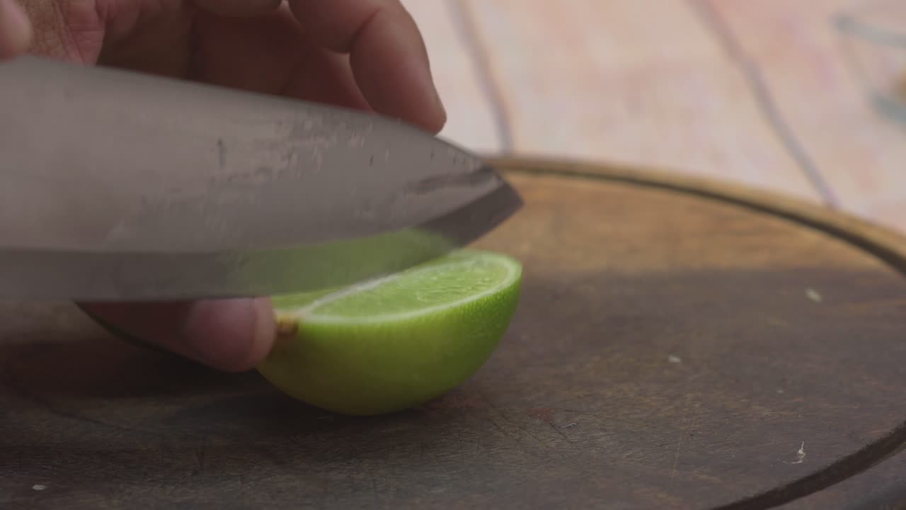 un primer plano extremo captura una mano cortando profesionalmente una lima fresca y húmeda, resaltando la ralladura y el detalle afilado del cuchillo metálico