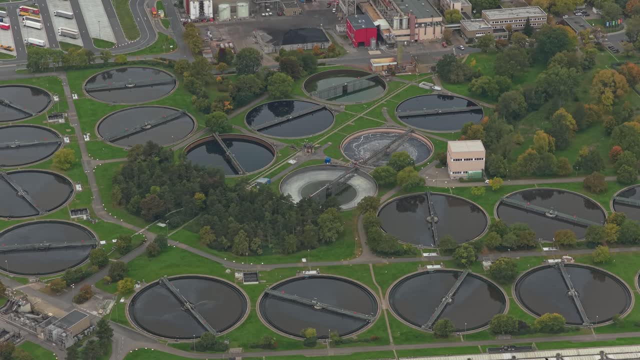 High angle aerial footage capturing the operations of a modern sewage treatment facility with large circular sedimentation tanks and water purification systems processing industrial wastewater