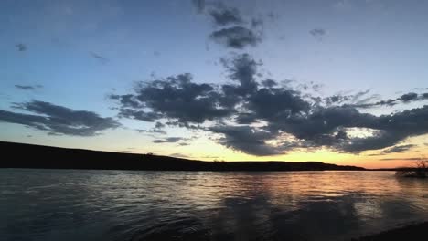 Zeitraffer-Eines-Flusses,-Nach-Einem-Sturm,-Mit-Wolken,-Sonnenuntergangsfarben-Und-Ruhigem-Fluss